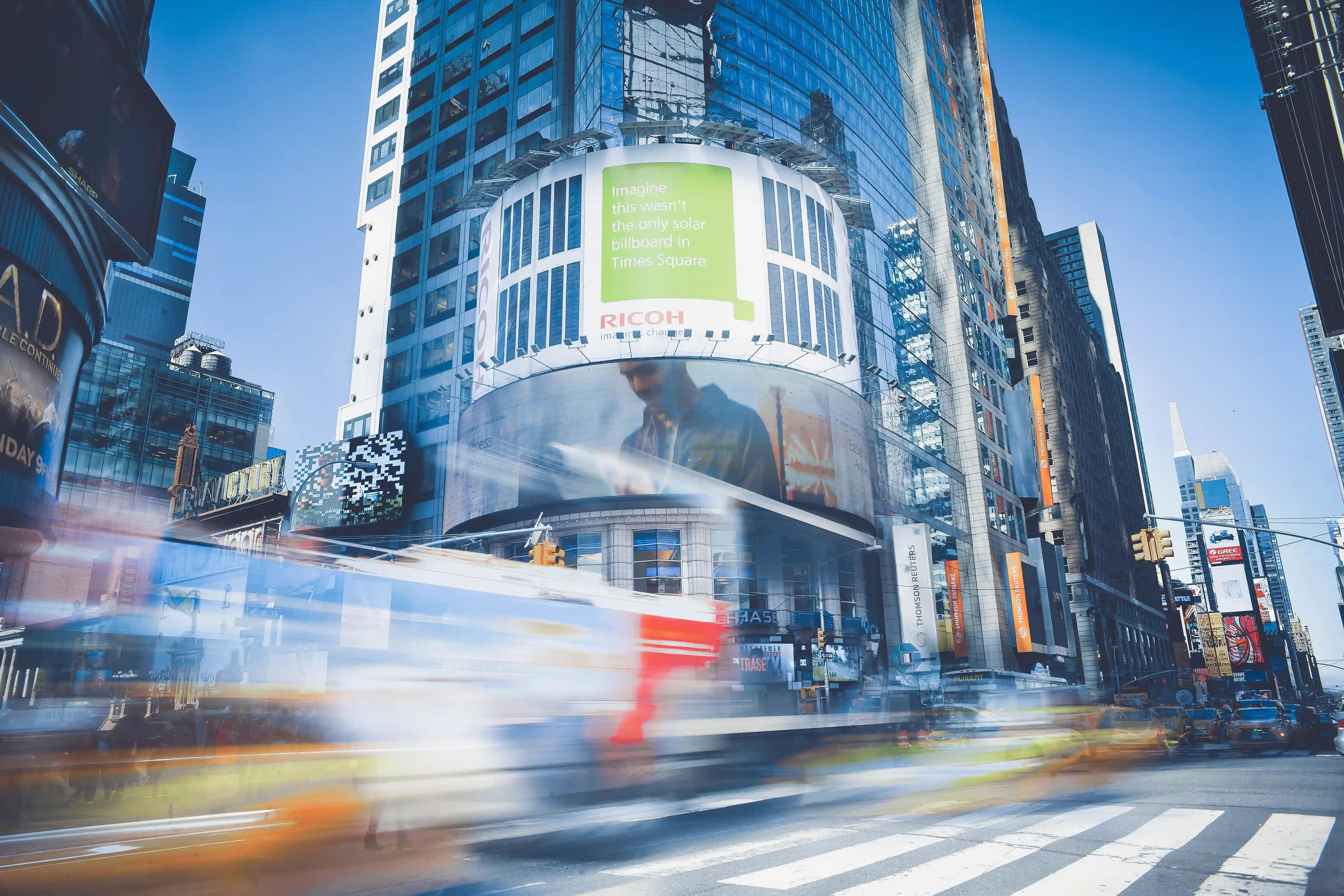 Photo of a street with busses and buildings in the background.